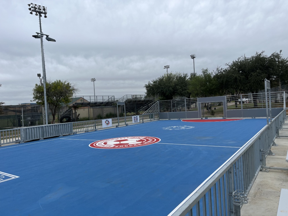 A photo of a blue mini pitch with a red and white soccer ball in the middle